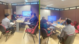 Na imagem, há uma sala de reunião com cinco pessoas sentadas em torno de uma mesa, em discussão,...