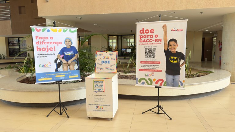 Pontos de Coleta do GACC no TRE-RN A foto mostra um baú ao centro da imagem e dois banners ao lado dele falam sobre o GACC. eles es...